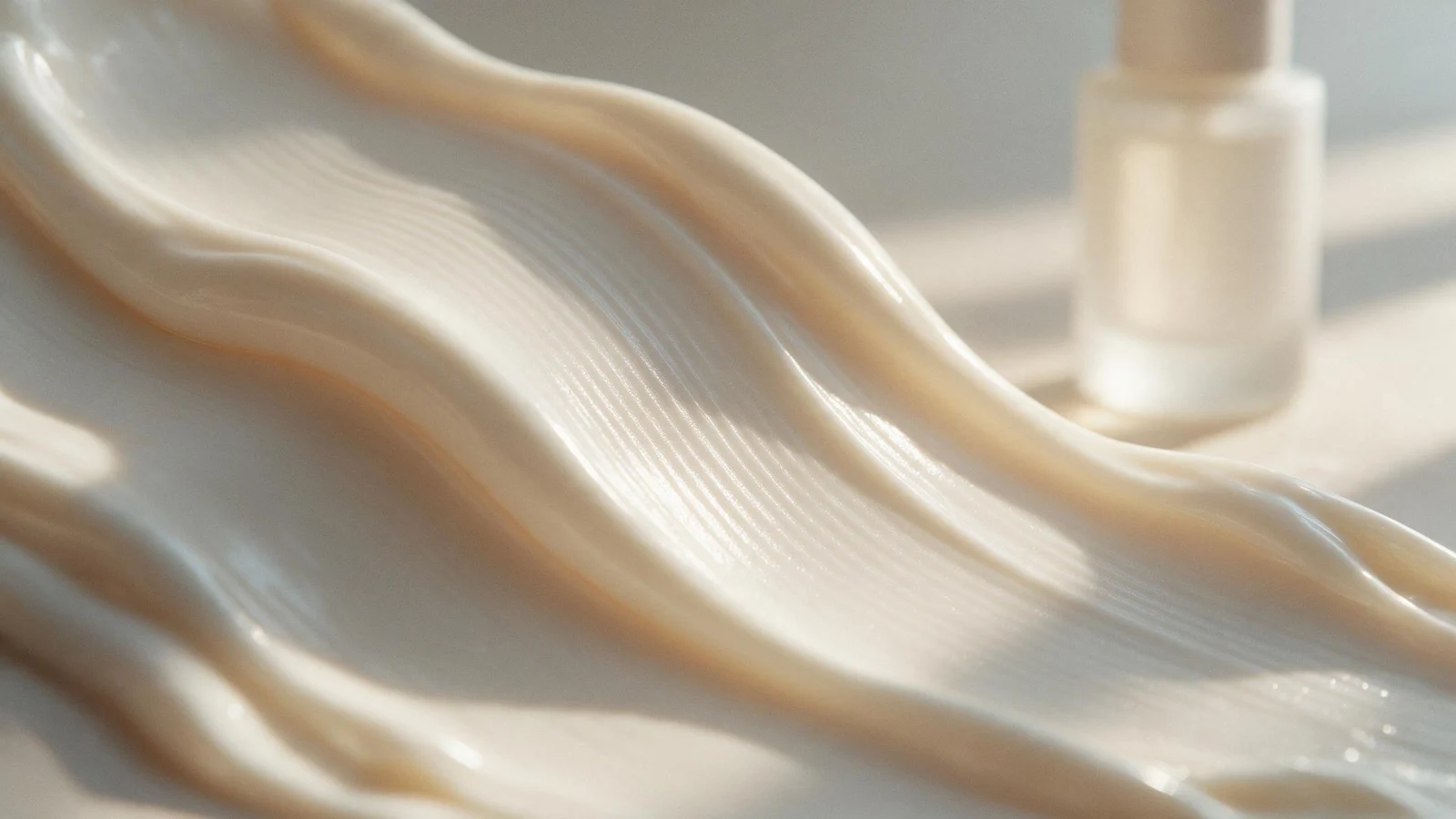 A glossy wave of cream with a single frosted glass bottle in the background